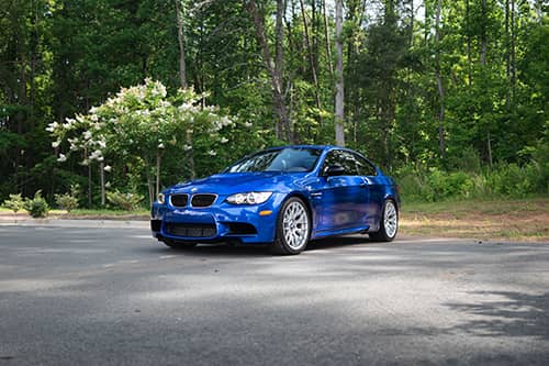 blue bmw parked in front of a forest of trees						
